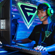 A student sits at a computer and plays a video game. There is a big "E" logo on the wall.